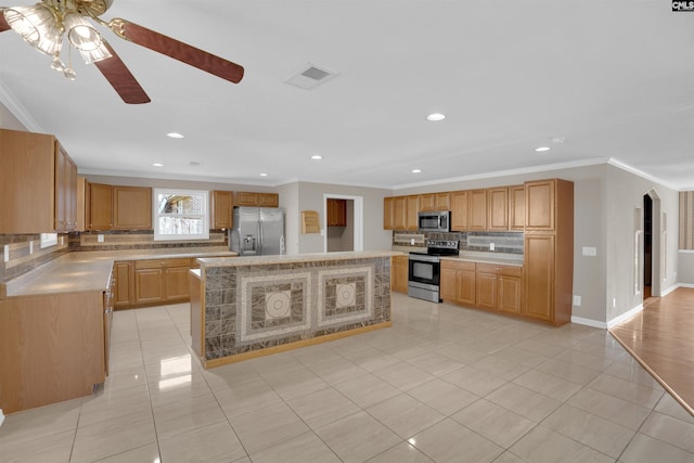 kitchen with stainless steel appliances, ornamental molding, a center island, and light tile patterned floors