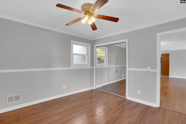 unfurnished bedroom featuring hardwood / wood-style flooring, ornamental molding, ceiling fan, and a closet