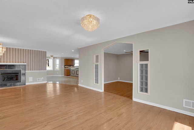 unfurnished living room with ceiling fan with notable chandelier, a tile fireplace, and light wood-type flooring