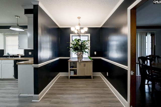 kitchen featuring pendant lighting, dishwasher, white cabinetry, ornamental molding, and a notable chandelier