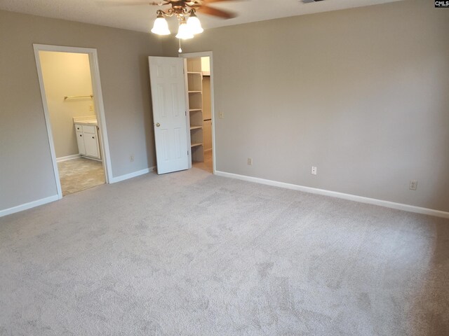 unfurnished bedroom featuring ceiling fan, connected bathroom, a walk in closet, light colored carpet, and a closet