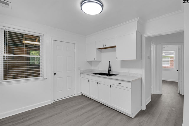 kitchen with white cabinetry, sink, ornamental molding, and light hardwood / wood-style floors