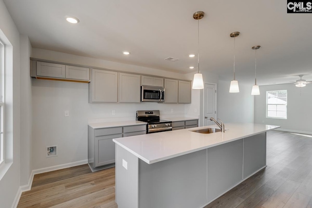 kitchen featuring sink, decorative light fixtures, stainless steel appliances, and a center island with sink