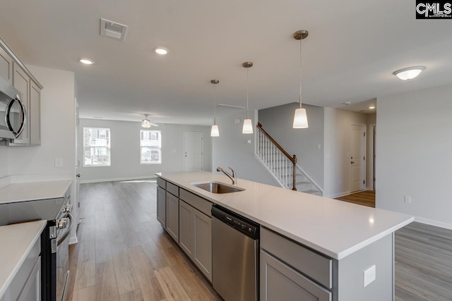 kitchen with decorative light fixtures, sink, gray cabinetry, stainless steel appliances, and a center island with sink