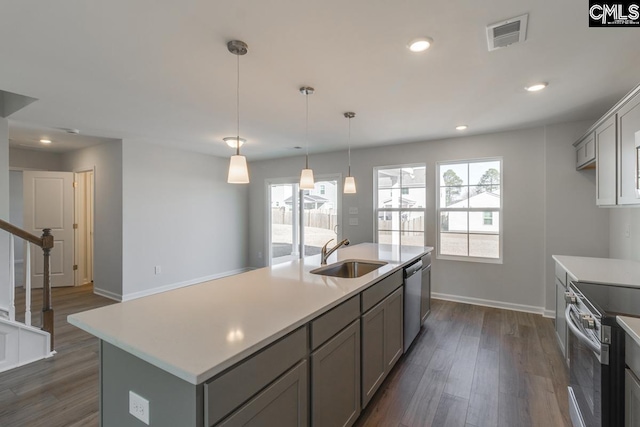 kitchen featuring sink, appliances with stainless steel finishes, gray cabinets, pendant lighting, and a kitchen island with sink