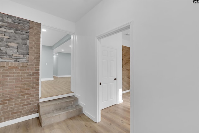 corridor featuring brick wall and light wood-type flooring