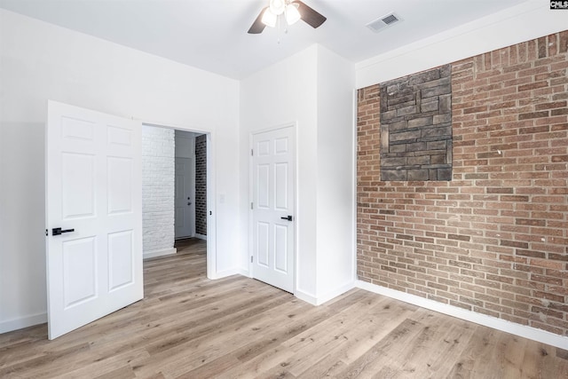 unfurnished bedroom featuring light wood-type flooring, ceiling fan, and brick wall