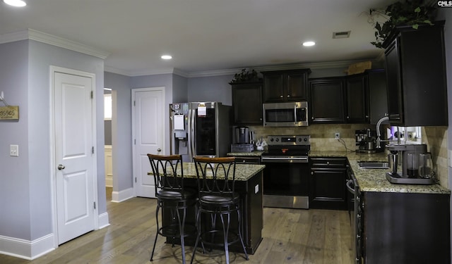 kitchen with a kitchen island, appliances with stainless steel finishes, a breakfast bar, wood-type flooring, and light stone counters