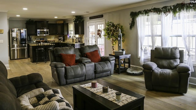 living room with french doors, crown molding, sink, and light wood-type flooring