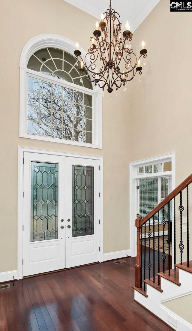 foyer with hardwood / wood-style flooring, a towering ceiling, an inviting chandelier, and french doors