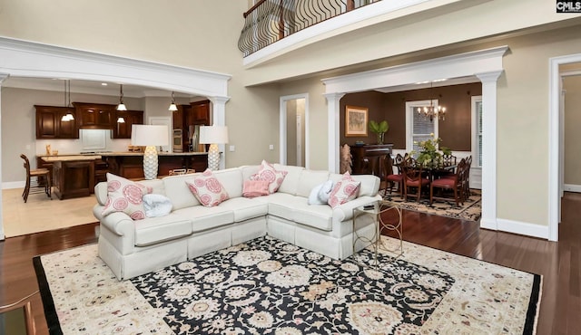 living room featuring a towering ceiling, dark wood-type flooring, a chandelier, and ornate columns