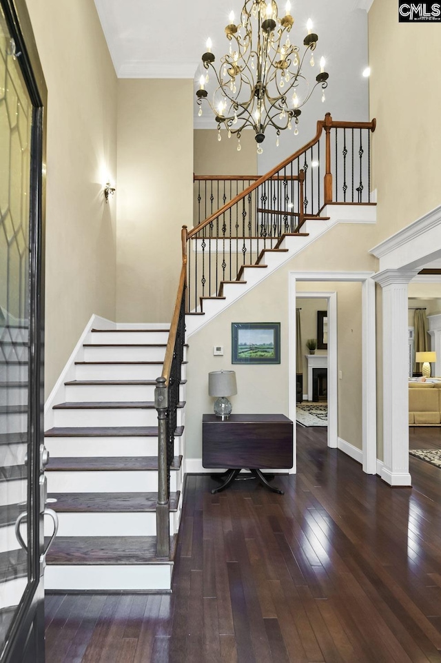 stairway with crown molding, hardwood / wood-style flooring, decorative columns, and a towering ceiling