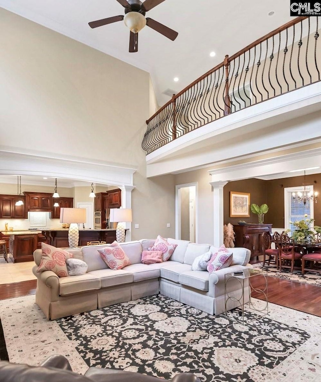 living room featuring a towering ceiling, ceiling fan with notable chandelier, and light hardwood / wood-style flooring