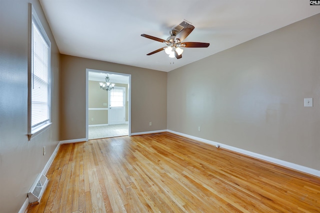 empty room with ceiling fan with notable chandelier, a healthy amount of sunlight, and light wood-type flooring