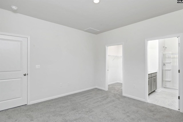 interior space with a walk in closet, connected bathroom, a closet, and light carpet