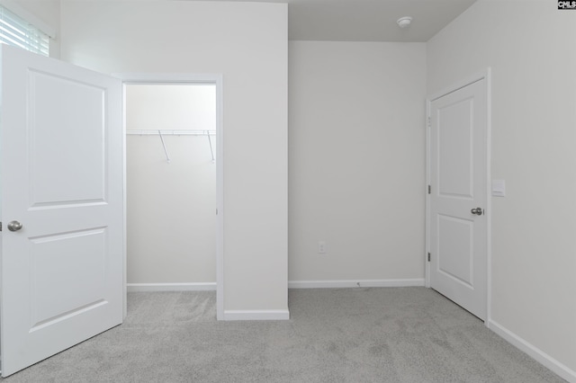 unfurnished bedroom featuring a walk in closet, light colored carpet, and a closet