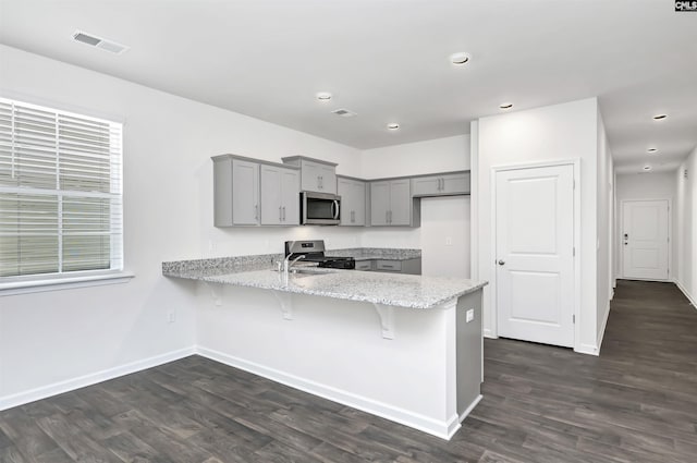 kitchen with stainless steel appliances, gray cabinetry, dark hardwood / wood-style flooring, and kitchen peninsula