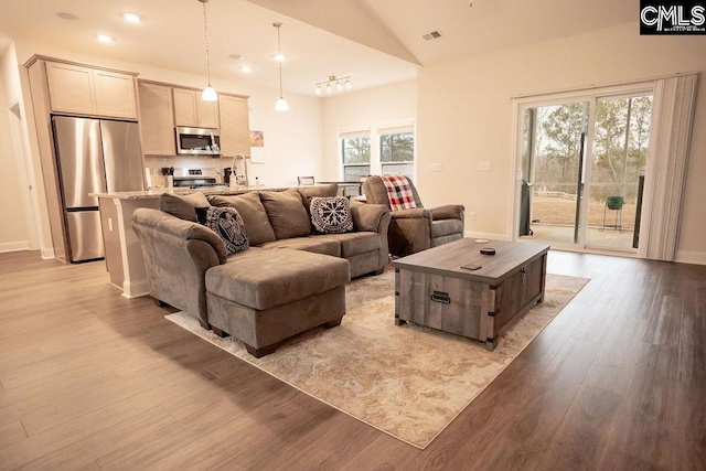 living room featuring sink, light hardwood / wood-style flooring, and vaulted ceiling