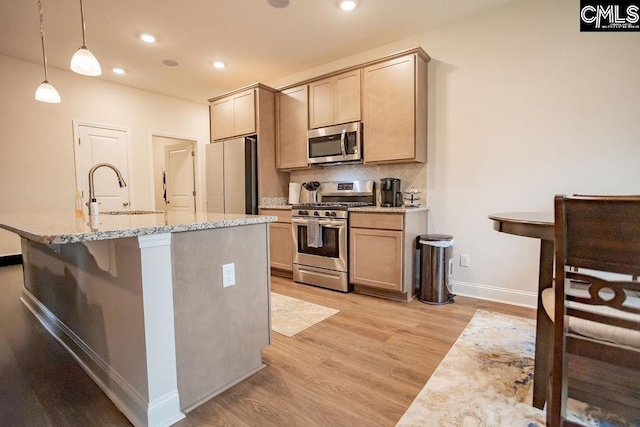 kitchen with light brown cabinetry, sink, decorative light fixtures, stainless steel appliances, and a kitchen island with sink