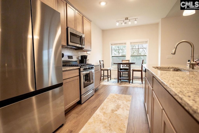 kitchen with appliances with stainless steel finishes, light brown cabinetry, sink, light stone counters, and light hardwood / wood-style floors