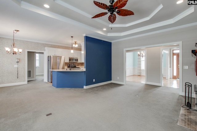 unfurnished living room with crown molding, ceiling fan with notable chandelier, light carpet, and a tray ceiling