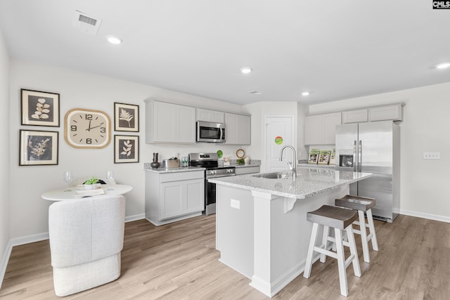 kitchen with sink, a breakfast bar area, light stone counters, appliances with stainless steel finishes, and a kitchen island with sink