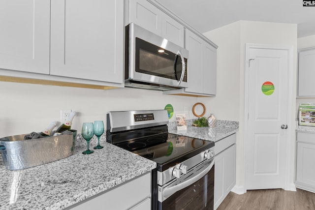 kitchen with light stone counters, light hardwood / wood-style flooring, stainless steel appliances, and white cabinets