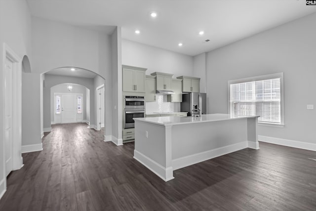 kitchen with gray cabinets, dark hardwood / wood-style floors, backsplash, stainless steel appliances, and a center island with sink