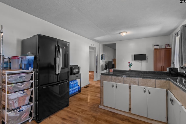 kitchen with a textured ceiling, white cabinets, light wood-type flooring, and black appliances