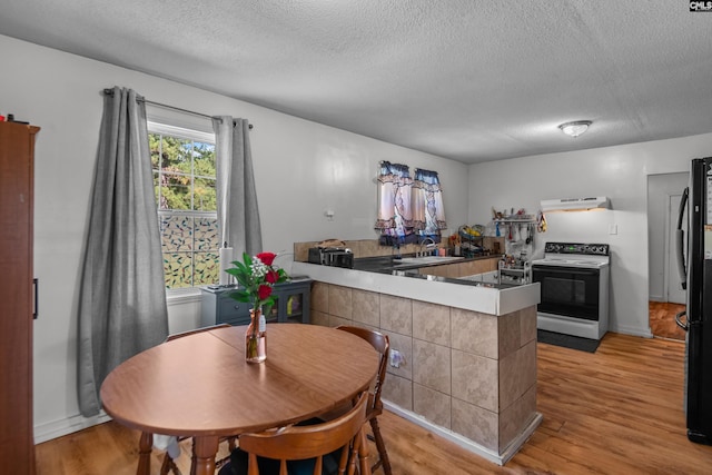 kitchen with electric range oven, black refrigerator, light hardwood / wood-style floors, kitchen peninsula, and a textured ceiling