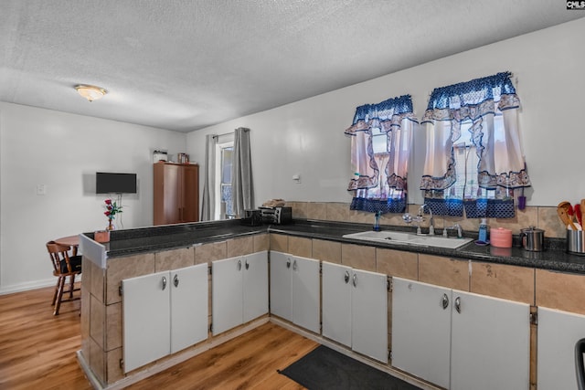 kitchen featuring white cabinetry, sink, light hardwood / wood-style flooring, and a textured ceiling