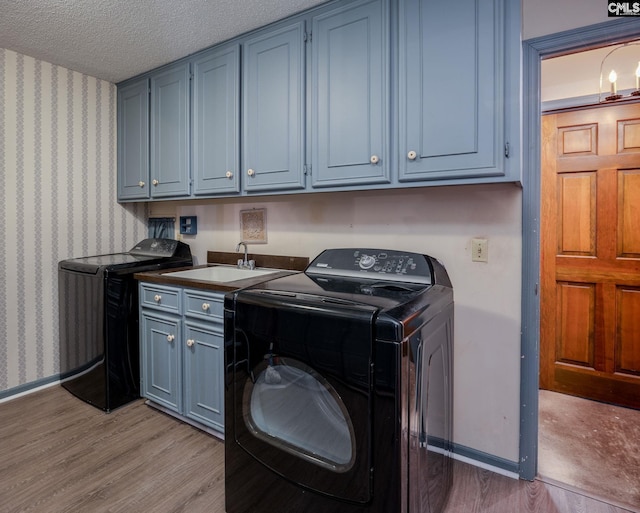 clothes washing area featuring sink, light hardwood / wood-style flooring, cabinets, a textured ceiling, and separate washer and dryer