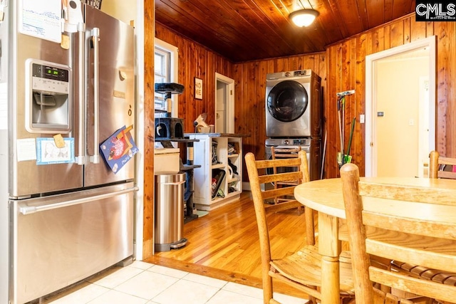 tiled dining room featuring stacked washer / dryer, wooden ceiling, and wood walls