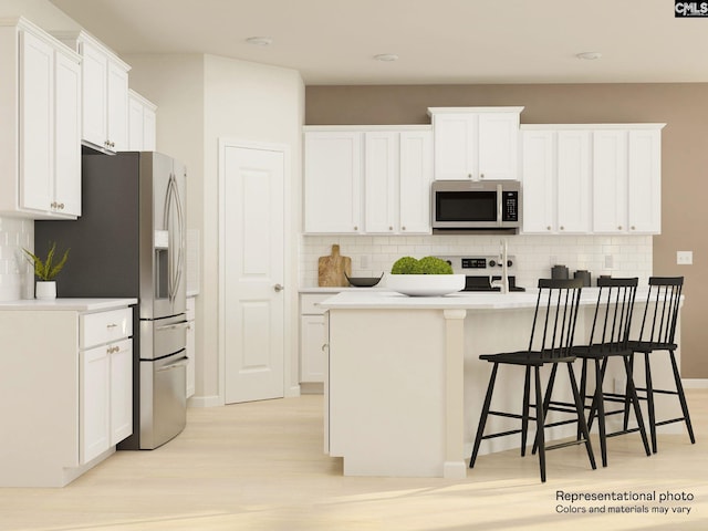 kitchen with an island with sink, appliances with stainless steel finishes, white cabinets, and light hardwood / wood-style flooring