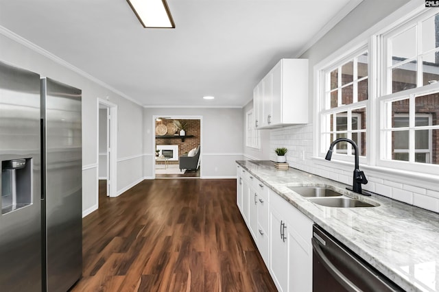 kitchen featuring a fireplace, white cabinetry, sink, ornamental molding, and stainless steel appliances