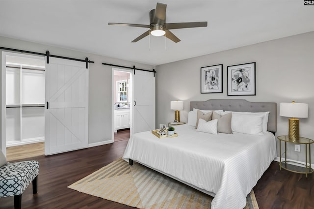 bedroom featuring dark hardwood / wood-style flooring, ceiling fan, a barn door, ensuite bath, and a closet