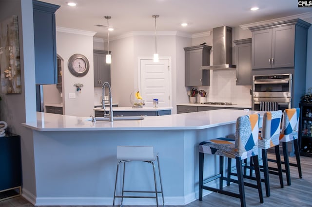 kitchen with wall chimney exhaust hood, a kitchen bar, decorative light fixtures, kitchen peninsula, and stainless steel appliances