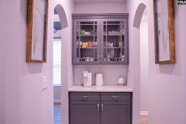 bar featuring decorative backsplash, gray cabinets, a healthy amount of sunlight, and hardwood / wood-style flooring