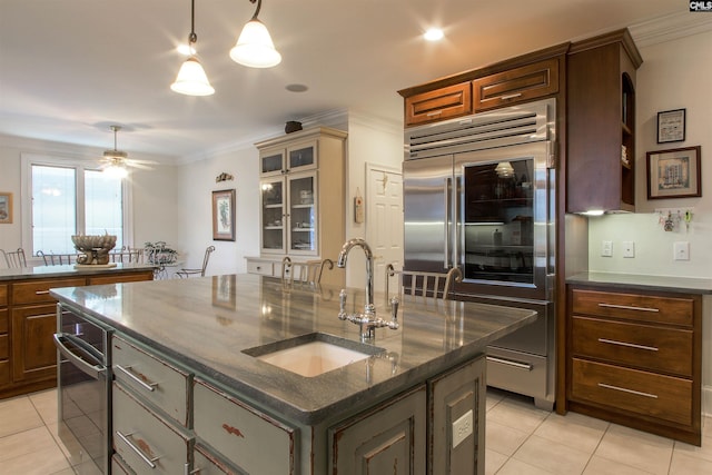 kitchen featuring crown molding, built in refrigerator, sink, and a kitchen island with sink