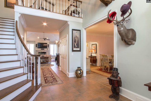 foyer entrance with ceiling fan, a towering ceiling, ornamental molding, and tile patterned flooring