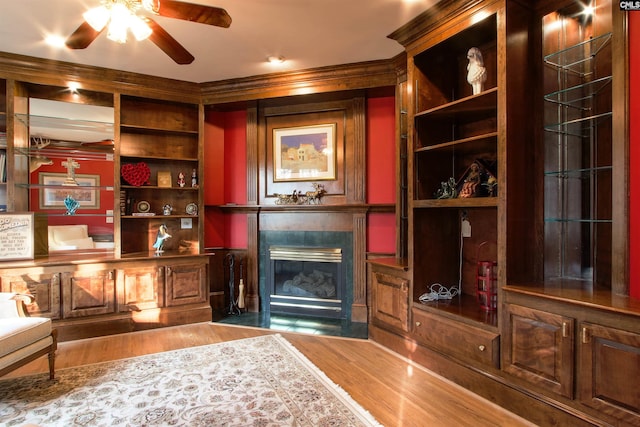 interior space featuring crown molding, built in features, ceiling fan, a premium fireplace, and hardwood / wood-style floors