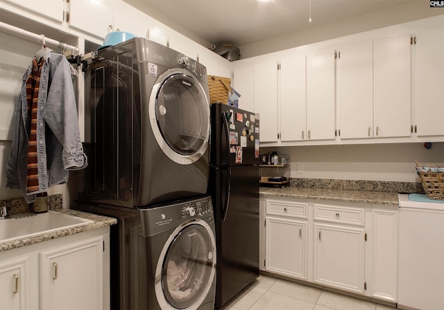 clothes washing area featuring light tile patterned floors, sink, cabinets, and stacked washer / dryer