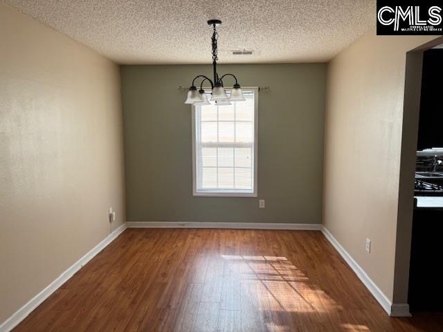 unfurnished dining area with an inviting chandelier, hardwood / wood-style flooring, and a textured ceiling