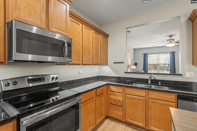 kitchen featuring sink, dark stone counters, ceiling fan, stainless steel appliances, and light hardwood / wood-style flooring