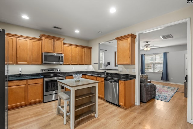 kitchen with stainless steel appliances, a kitchen island, sink, and light hardwood / wood-style floors