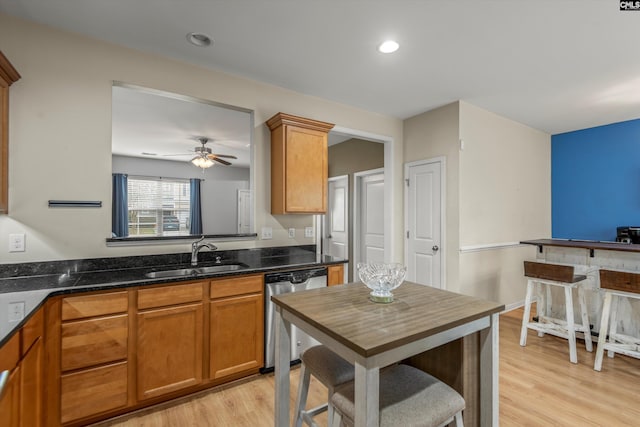 kitchen featuring sink, light hardwood / wood-style flooring, stainless steel dishwasher, ceiling fan, and dark stone counters