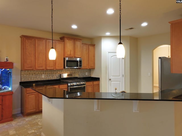 kitchen with pendant lighting, appliances with stainless steel finishes, a kitchen breakfast bar, a center island with sink, and decorative backsplash