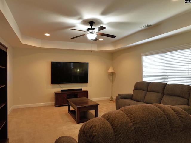 living room with ceiling fan, a tray ceiling, and light carpet