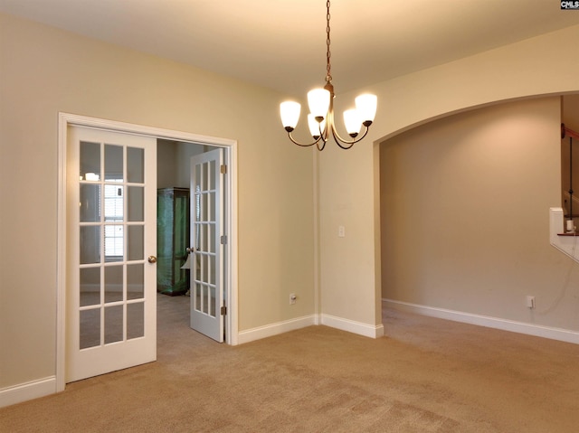 carpeted empty room featuring an inviting chandelier and french doors