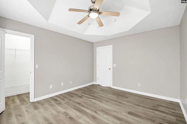 unfurnished bedroom with wood-type flooring, a spacious closet, a raised ceiling, a closet, and ceiling fan